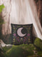 Black woven throw pillow with an embroidered crescent moon and floral pattern in soft ivory, green, purple, and gold, featuring a textured finish.